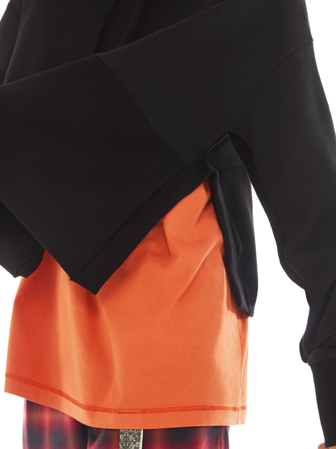 detail of black poncho with maxi slit on the side with orange t-shirt under